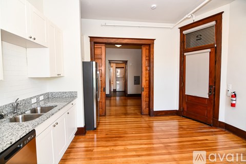 A kitchen with white cabinets and a wooden floor leading to a hallway.