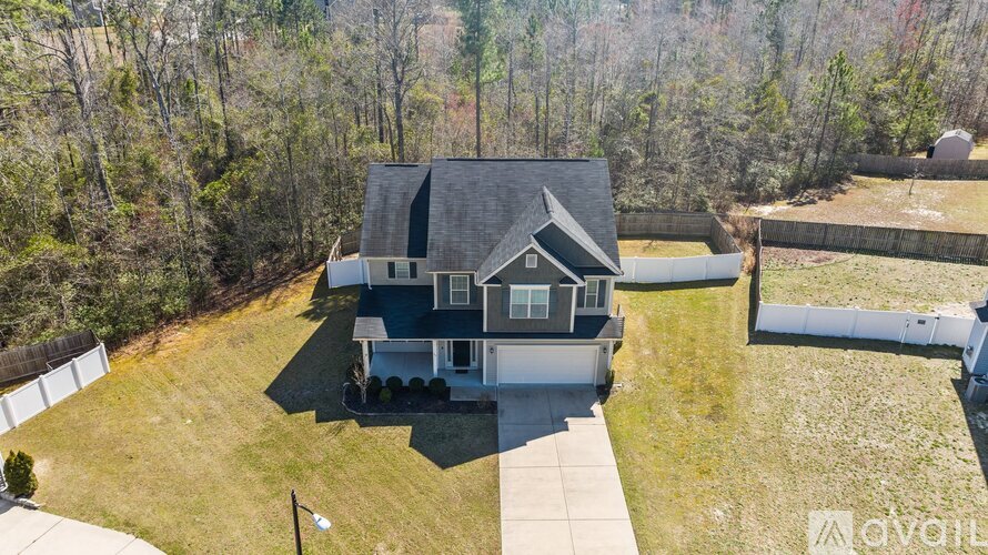 A house with a grey roof and a white fence is surrounded by trees.