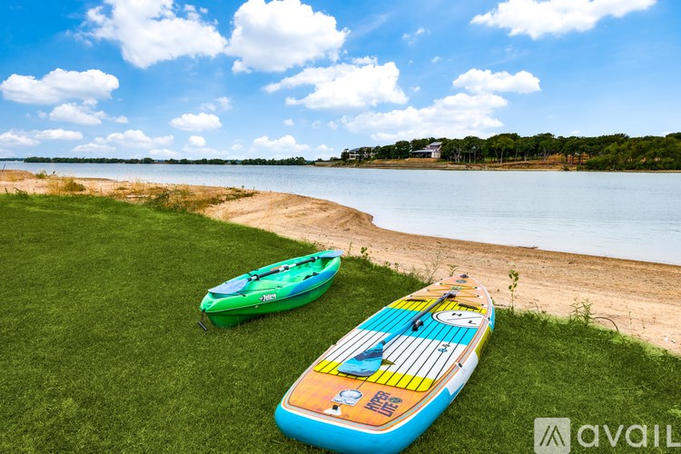 Two kayaks are on the grass by the water.
