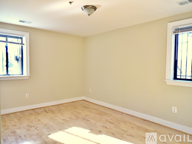 A room with wooden flooring and two windows.