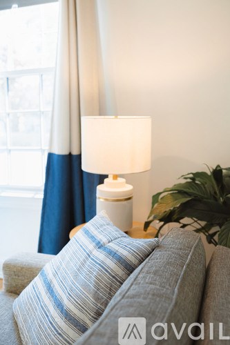 A lamp with a white shade is on a table next to a couch with blue and white striped pillows.