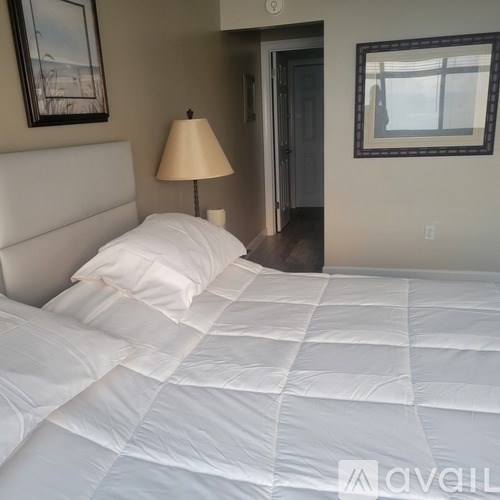 A bed with white sheets and a white headboard with a lamp on a side table.