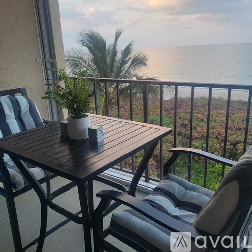 A balcony with a table and chairs overlooking the ocean.