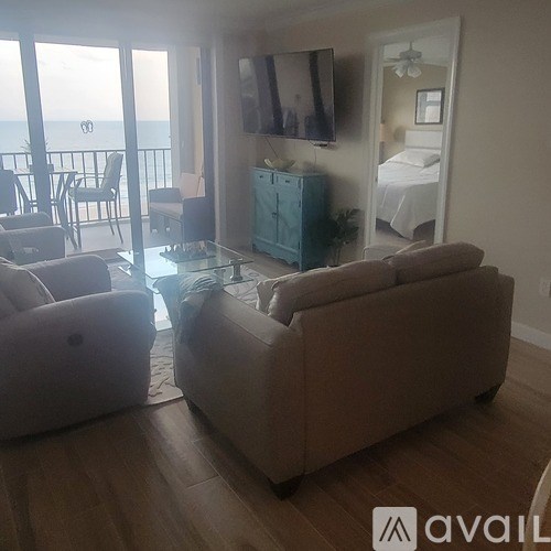 A living room with a couch, chair, and a balcony overlooking the ocean.