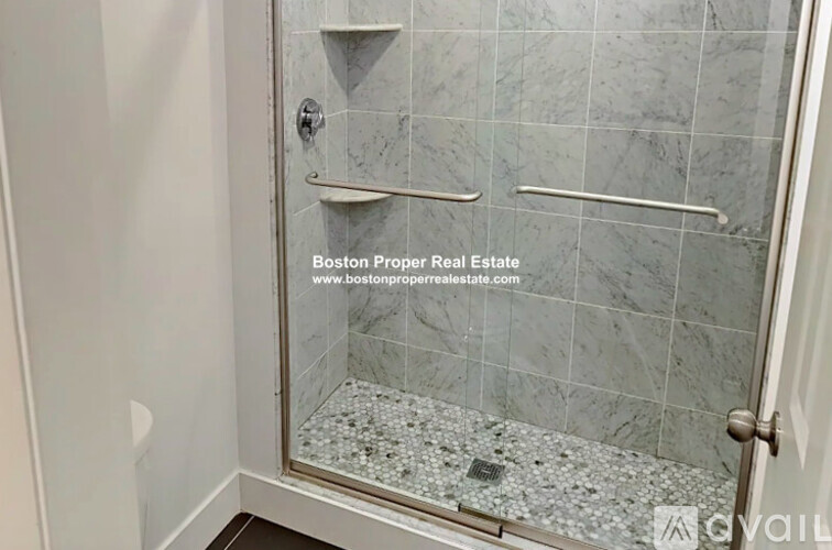 A shower area with a glass door and a marble tile floor.