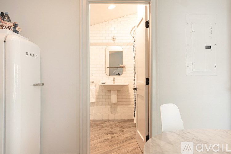 A white refrigerator is in the corner of a room with a bathroom visible through the open door.