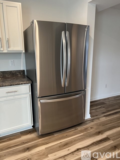 A stainless steel refrigerator in a kitchen with wooden floors.