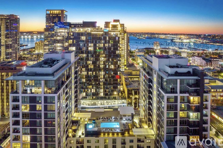 A cityscape at dusk with a large building in the foreground and a body of water in the background.