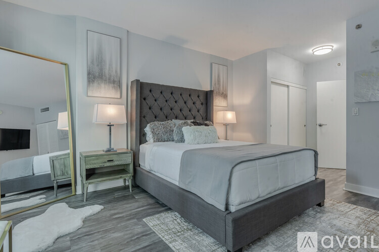 A bedroom with a large bed, a mirror, and a nightstand with a lamp.