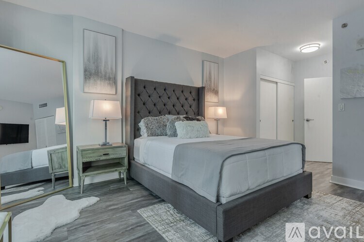 A bedroom with a large bed, a mirror, and a nightstand with a lamp.