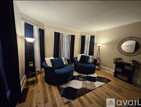 A living room with two blue chairs and a round mirror on the wall.