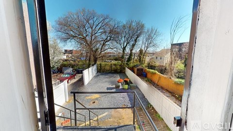 A view from a window looking out to a gravel area with trees and buildings in the distance.