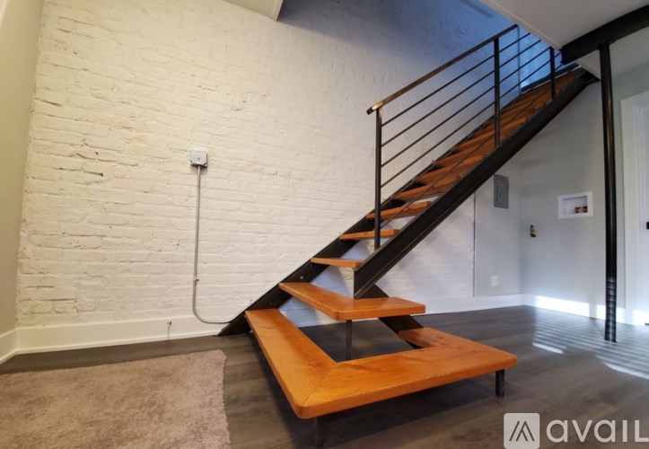 A wooden staircase with a metal railing leads up to a white wall.