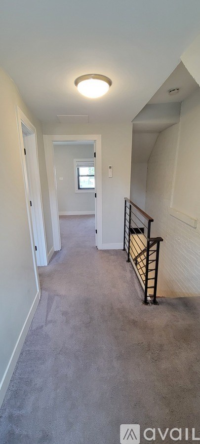 A long hallway with a light on the ceiling and a window in the distance.