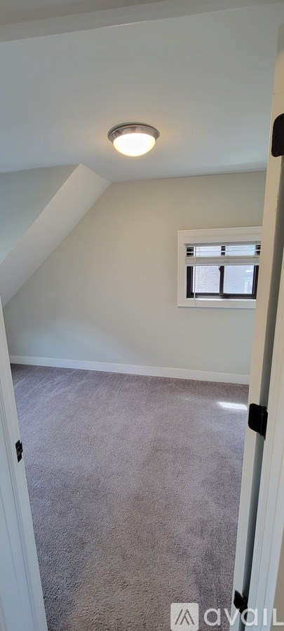 A carpeted room with a window and a light on the ceiling.