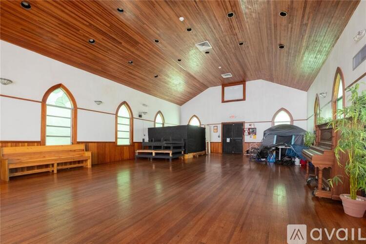 A spacious room with wooden floors and a high ceiling with windows on the side.
