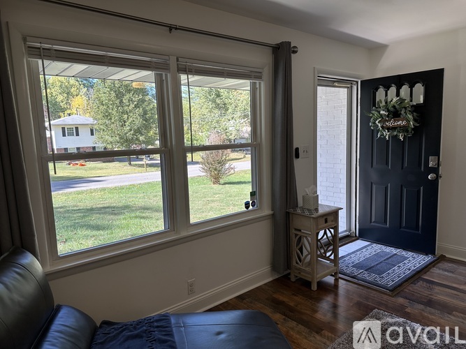 A room with a black door, a window with a view of a house and trees, and a wreath on the door.