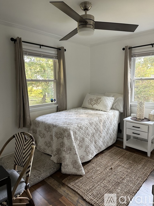 A bedroom with a bed, chair, and a ceiling fan.