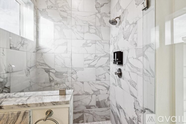 A shower area with a marble tile wall and a gold shower drain.
