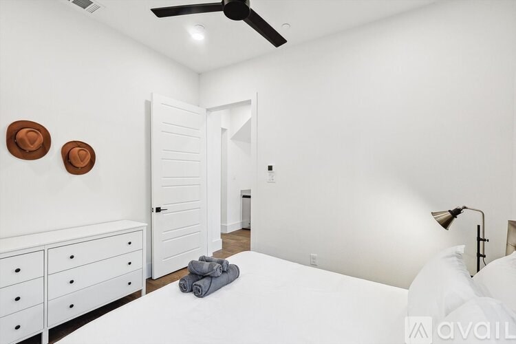 A bedroom with a white bed, a white dresser, and a white ceiling fan.