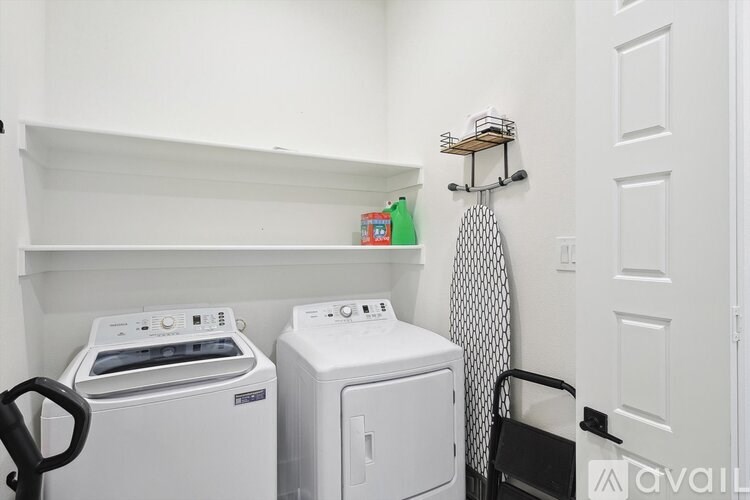 A laundry room with a washer and dryer, a shelf, and a black chair.