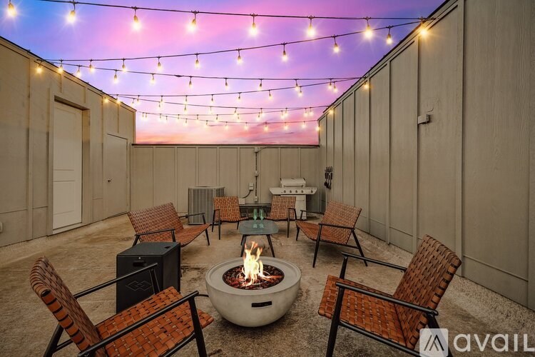 A patio with a fire pit and chairs under string lights.