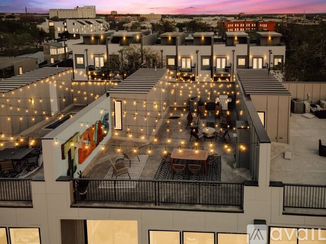 A rooftop patio with tables and chairs is lit up with string lights.
