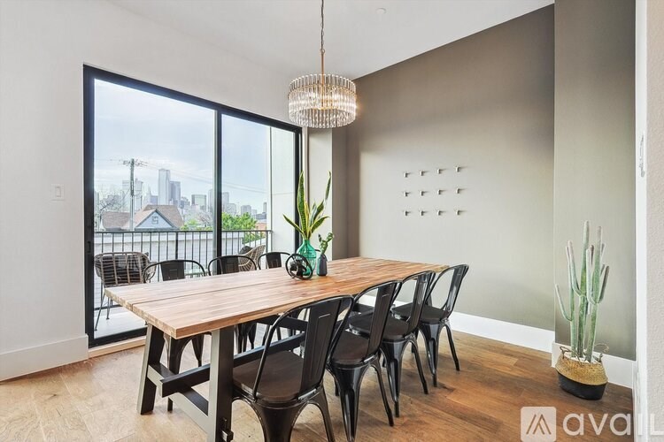 A dining room with a wooden table and chairs, a potted plant, and a view of the city through the window.