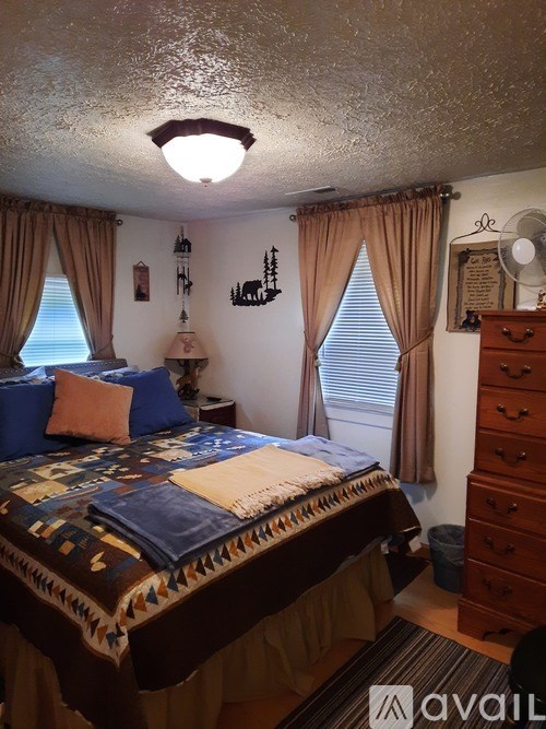 A bedroom with a bed, dresser, and window with curtains.