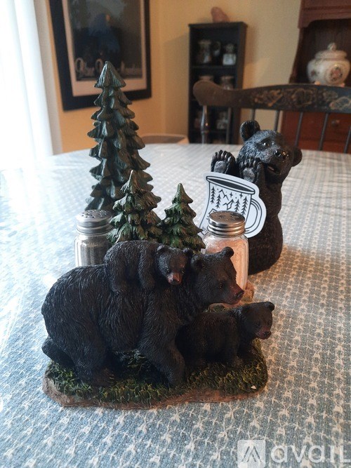A black bear family is sitting on a table with a small Christmas tree and a mug.