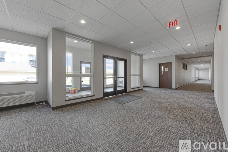 A spacious office room with a carpeted floor, a window, and a door.
