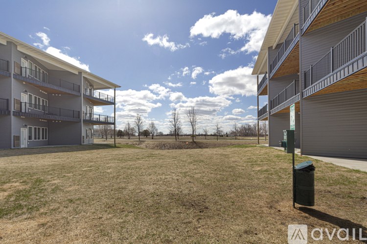 A grassy field with apartment buildings and a trash can in the foreground.