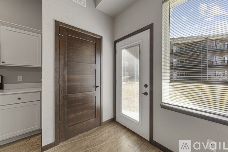 A wooden door is in a white room with a window.