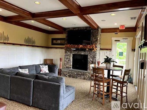 A living room with a grey couch, a wooden table and chairs, and a stone fireplace.