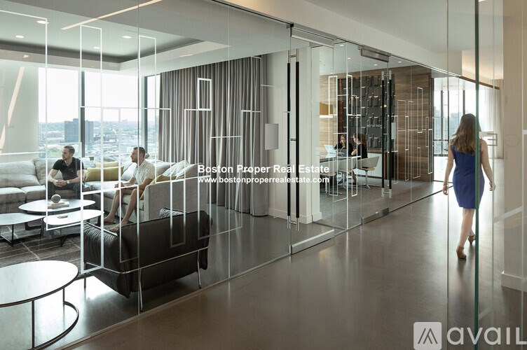 A modern living room with a glass wall and a woman walking towards it.