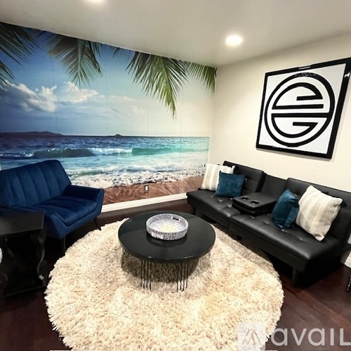 A living room with a beach scene on the wall and a black couch.