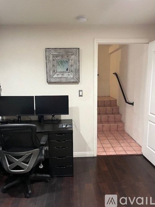 A black computer desk with a black chair and a painting on the wall.