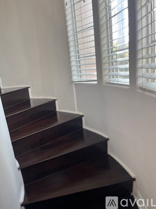 A staircase with a white wall and a window with blinds.