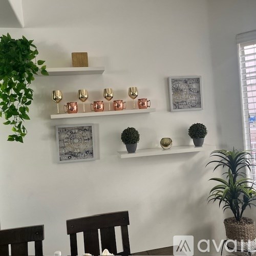 A living room with a white wall, a wooden bench, a potted plant, and a shelf with decorative items.