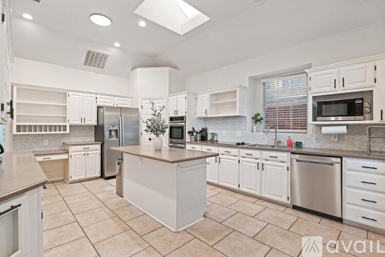 A kitchen with white cabinets and appliances, a large island in the middle, and a tiled floor.