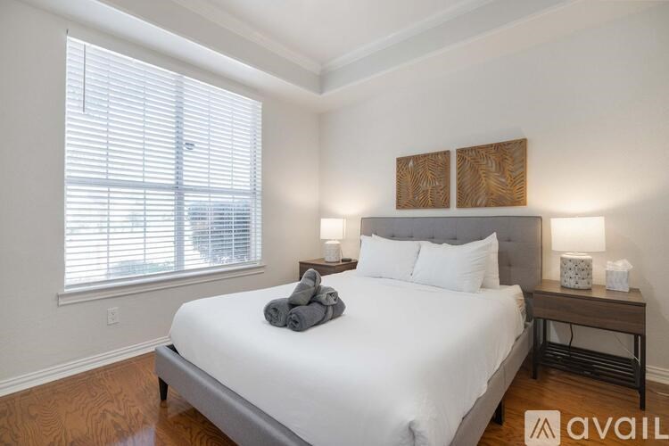 A bedroom with a large bed, a window with blinds, and a nightstand with a lamp.