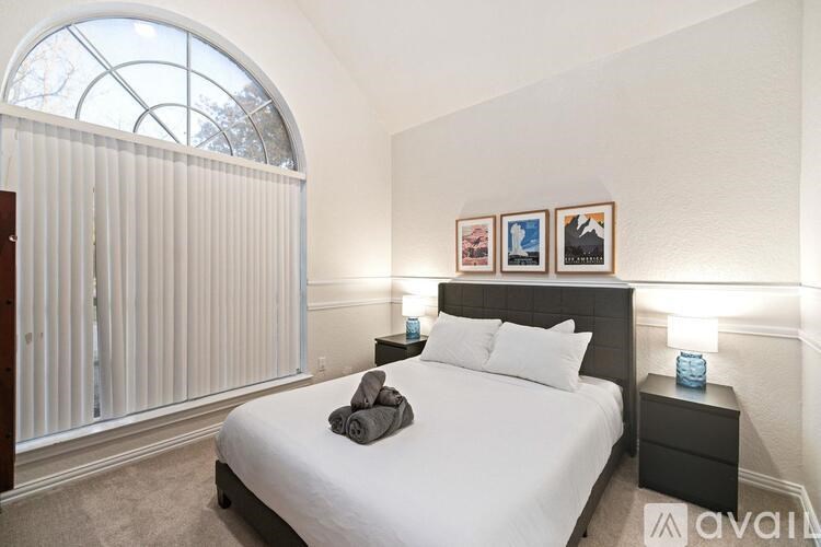 A bedroom with a large bed, a nightstand, and a window with blinds.