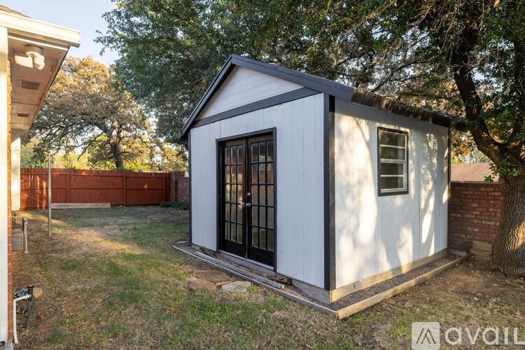 A small white house with a black door is surrounded by trees and grass.