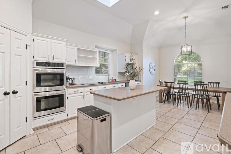 A kitchen with white cabinets and a large island with a trash can.