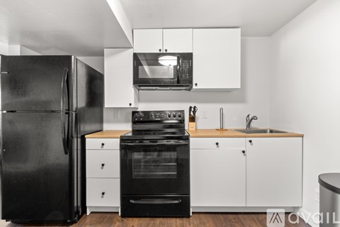 A black refrigerator is in a kitchen with white cabinets.