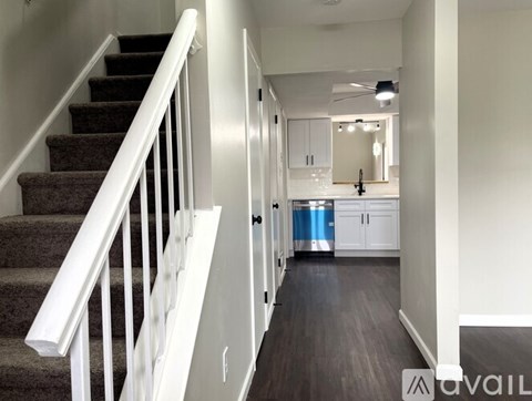 A staircase with a white railing leads to a kitchen area with white cabinets and a blue refrigerator.