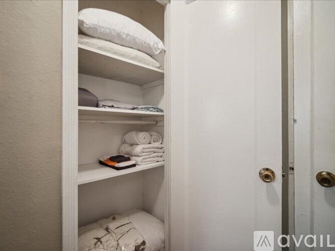 A white closet with a door and a shelf with towels and a book.