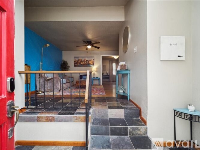 A red door opens to a hallway with a fan and a painting on the wall.