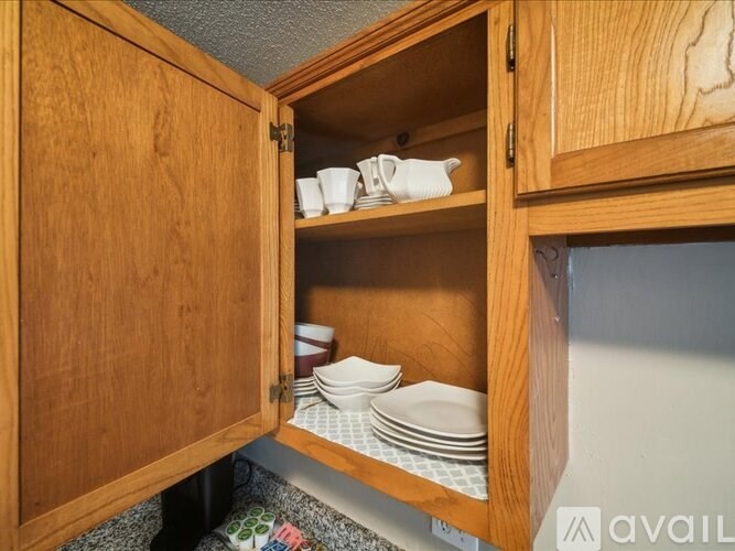 A kitchen cabinet is open, revealing white plates and bowls.
