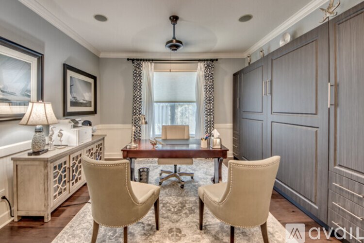 A well-lit room with a desk, chairs, and a painting on the wall.